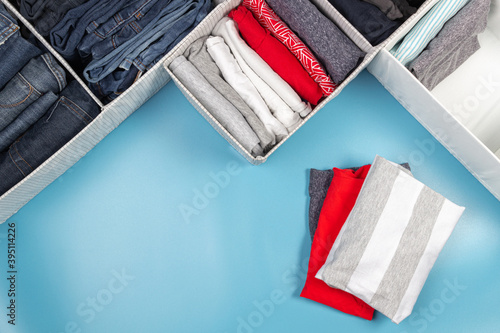 Vertical storage of clothing, tidying up, room cleaning concept. Stack of folded clothes in basket over light blue background. Top view photo