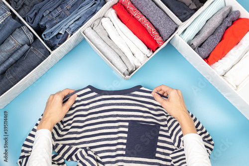 Female hands folds and puts clothes to baskets. Vertical storage of clothing, tidying up, room cleaning. Marie Kondo style of garments declutter and sorting. Top view photo