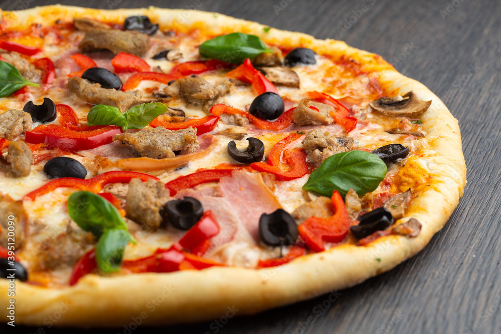 Italian pizza with melted mozzarella cheese, olives and sausage garnished with fresh vegetables and basil leaves Italian pizza with melted mozzarella cheese, olives and sausage garnished with fresh vegetables and basil leaves