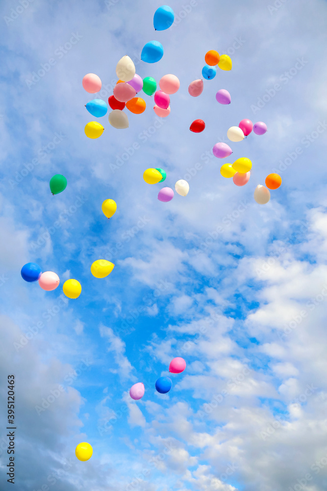 Balloons of different colors in the blue sky with clouds.