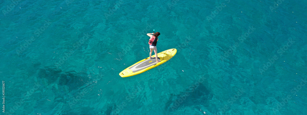 Aerial drone ultra wide top down photo of fit unidentified woman paddling on a SUP board or Stand Up Paddle in Mediterranean turquoise clear sea Aerial drone ultra wide top down photo of fit unidentified woman paddling on a SUP board or Stand Up Paddle in Mediterranean turquoise clear sea