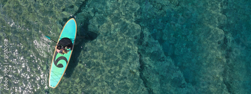 Aerial drone ultra wide top down photo of fit unidentified woman paddling on a SUP board or Stand Up Paddle in Mediterranean turquoise clear sea photo