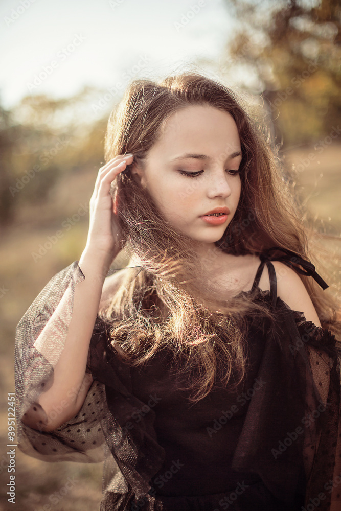 Naklejka premium girl stands in the park in autumn in the rays of the setting sun