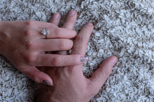 Two hands of a couple in love with an engagement ring placed on the bed. Marriage concept