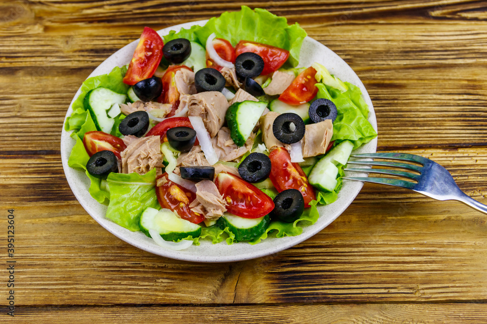 Tasty tuna salad with lettuce, black olives and fresh vegetables on wooden table Tasty tuna salad with lettuce, black olives and fresh vegetables on wooden table