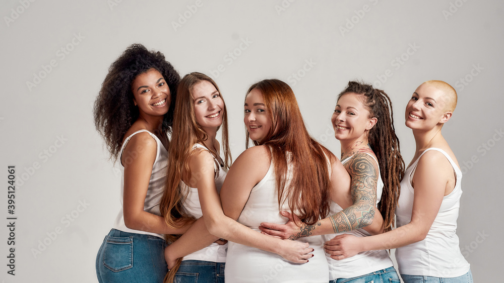Group of five beautiful diverse young women wearing white shirt and denim  jeans putting arms around each other, looking at camera while posing  together isolated over grey background Stock Photo | Adobe