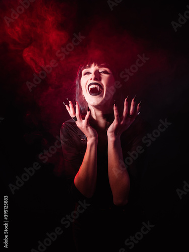 Raising her hands to her face, a woman in the guise of a vampire laughs ominously into the camera while showing long fangs.