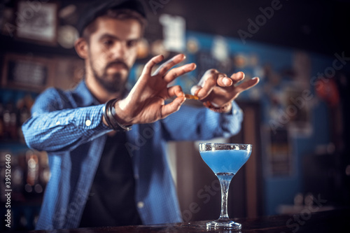 Bearded bartender places the finishing touches on a drink while standing near the bar counter in nightclub photo