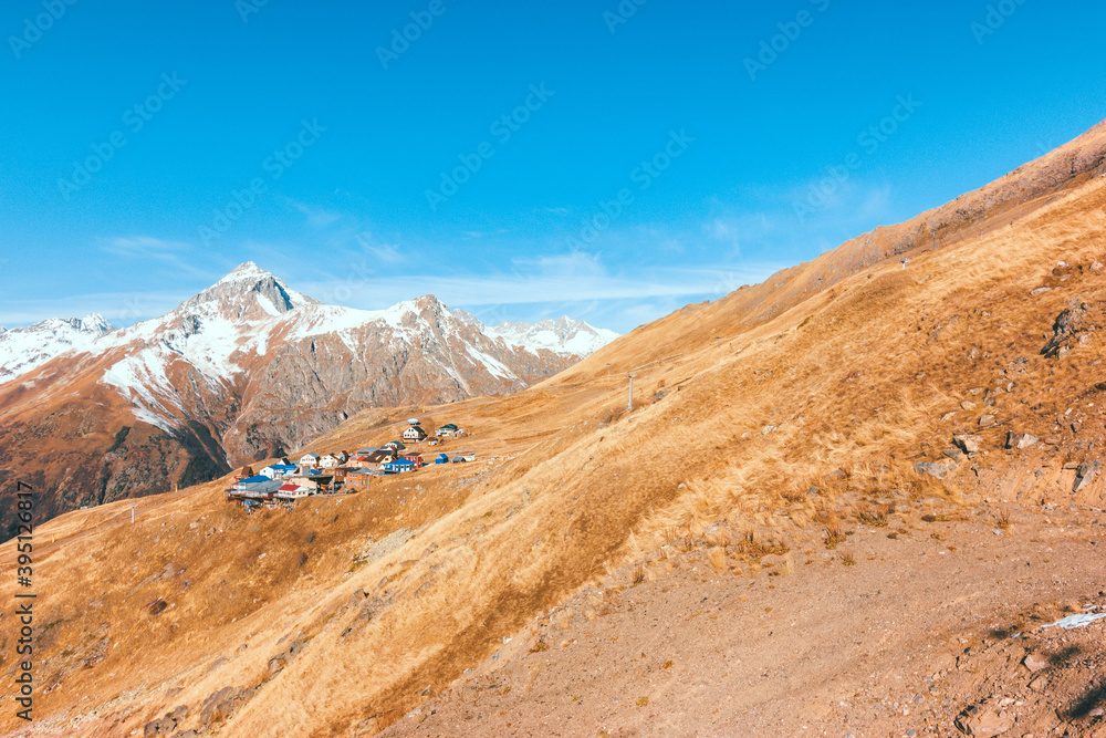 Village on the mountainside in autumn. Ski resort in the off-season. Snowy peaks on a sunny day, Dombay