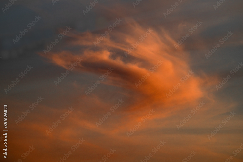 An orange cloud floats in the sky during sunset