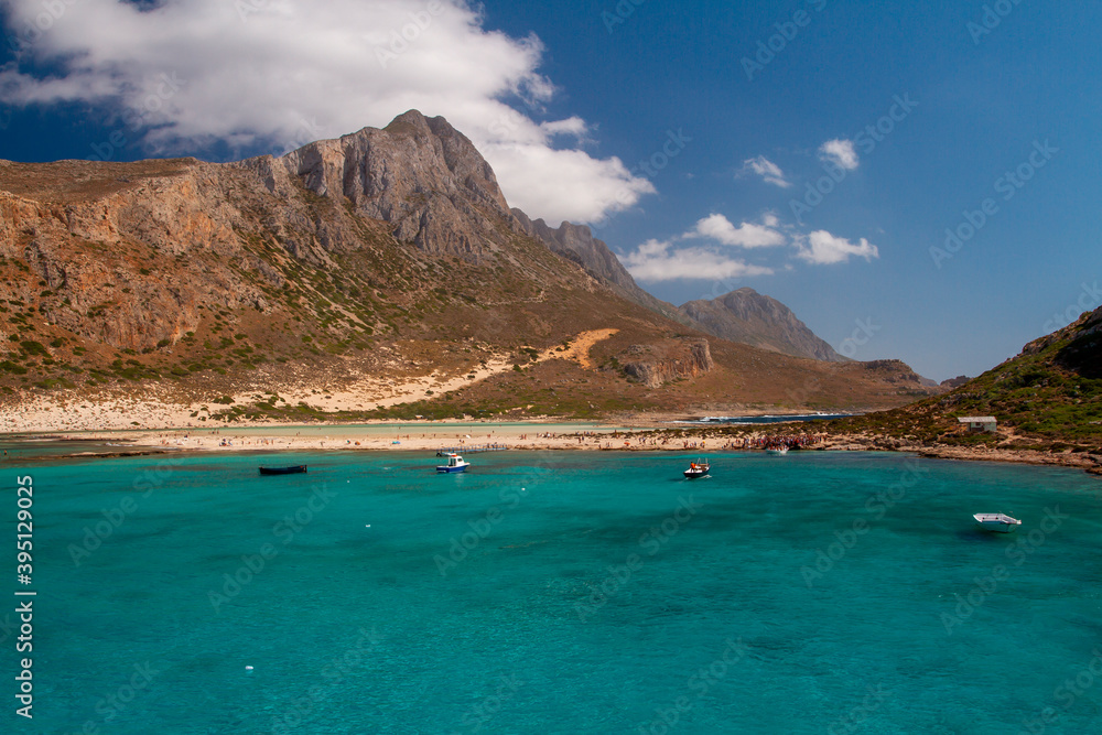 Fototapeta premium the surface of the clear sea and in the background is a mountain and blue sky with white clouds in Greece during the day and a sailing ship on the surface