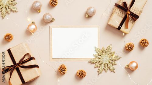 Christmas card mockup on pastel beige background with gift boxes, golden balls and xmas decorations. Flat lay, top view. Minimal style.