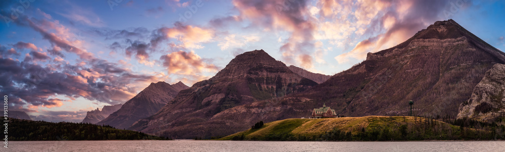 Iconic Hotel in Glacier Lake surrounded by the beautiful Canadian Rocky Mountains during a cloudy summer sunset. Taken in Upper Waterton Lake, Alberta, Canada.