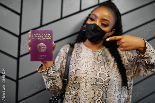 African woman wearing black face mask show Ethiopia passport in hand. Coronavirus in Africa country, border closure and quarantine, virus outbreak concept.