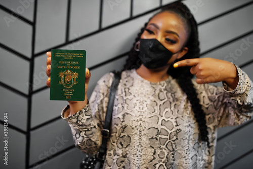 African woman wearing black face mask show Ivory Coast passport in hand. Coronavirus in Africa country, border closure and quarantine, virus outbreak concept. photo