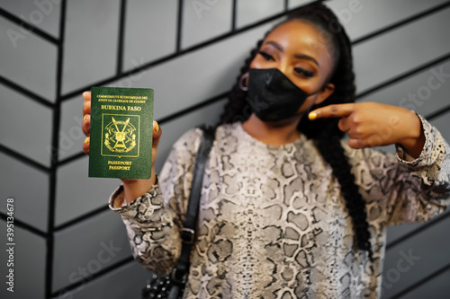 African woman wearing black face mask show Burkina Faso passport in hand. Coronavirus in Africa country, border closure and quarantine, virus outbreak concept.