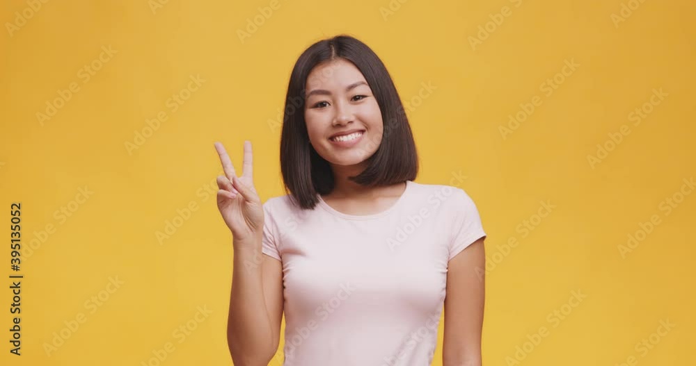 Young positive asian woman showing peace gesture, expressing fun and happiness, orange studio background Young positive asian woman showing peace gesture, expressing fun and happiness, orange studio background