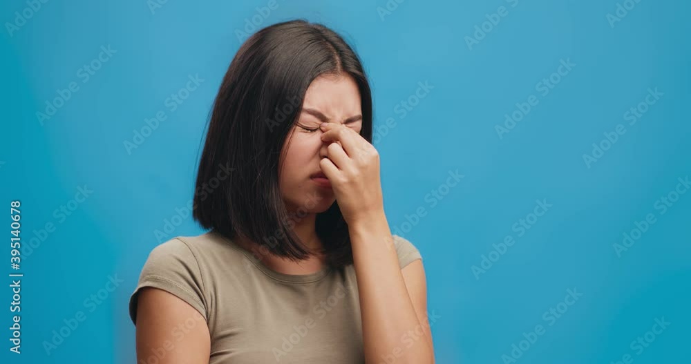 Stressed young asian woman having terrible headache attack, massaging nose bridge, blue studio background Stressed young asian woman having terrible headache attack, massaging nose bridge, blue studio background