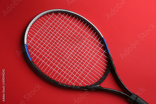 Tennis racket on red background, top view. Sports equipment