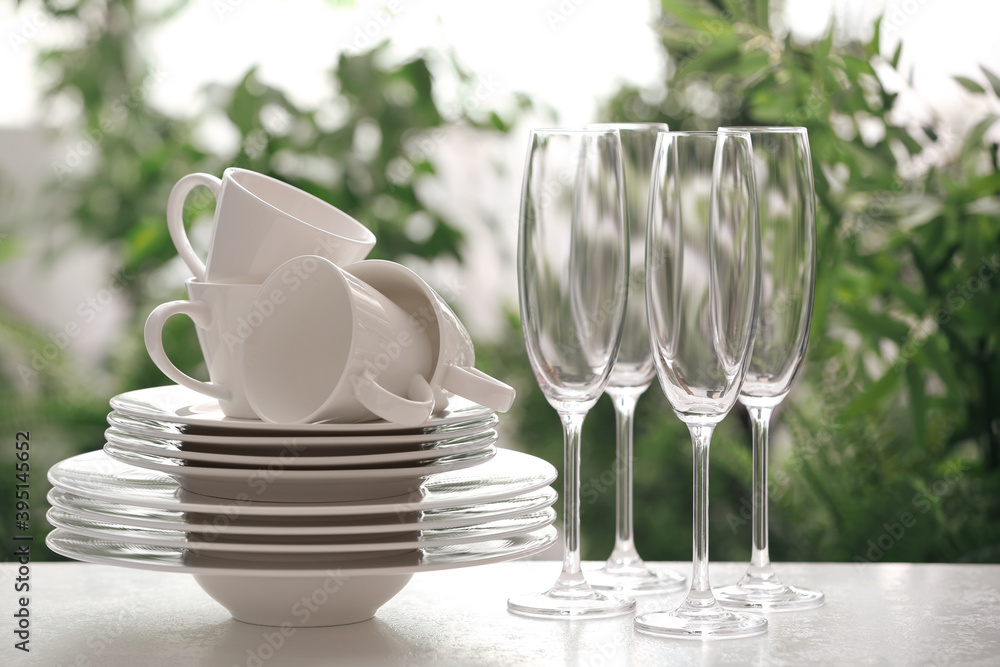 Set of clean dishware and champagne glasses on white table against blurred background