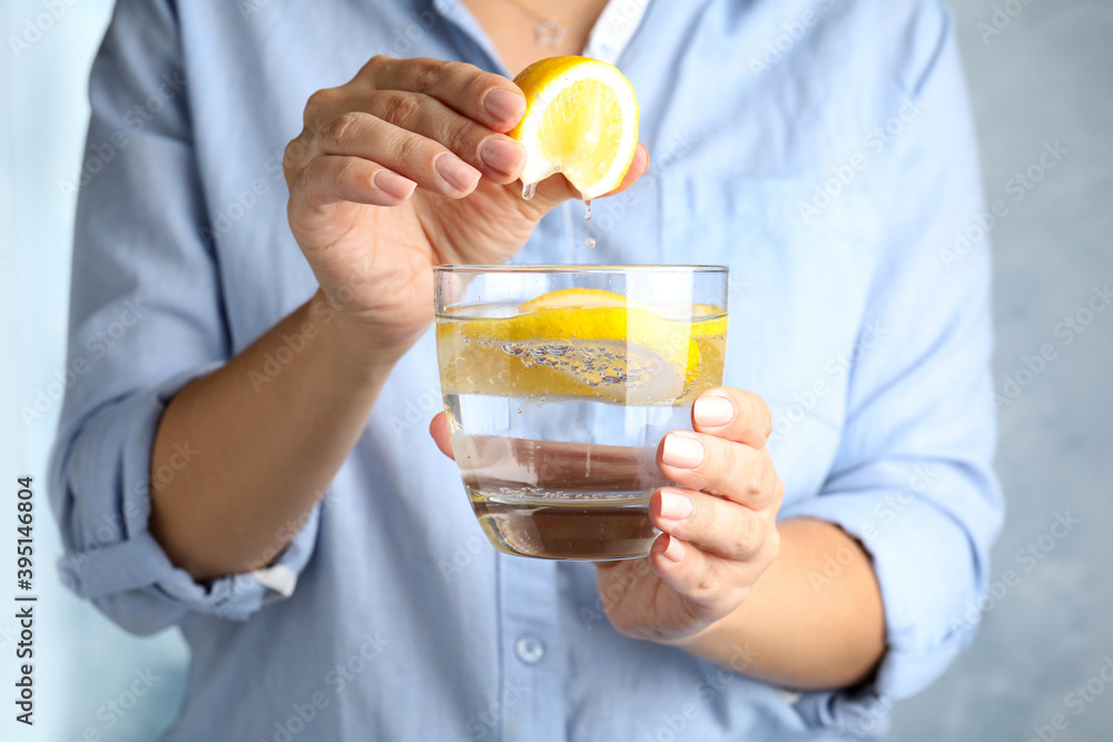 Woman squeezing lemon juice into glass of soda water, closeup Woman squeezing lemon juice into glass of soda water, closeup