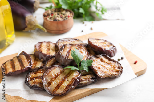 Delicious grilled eggplant slices with parsley and spices on white wooden table, closeup