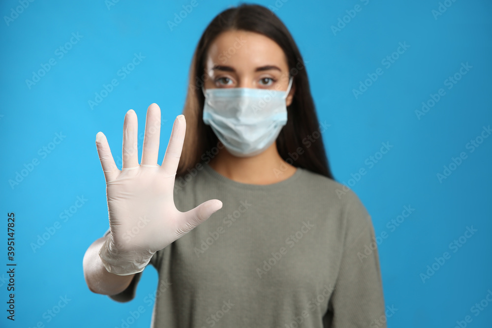 Woman in protective face mask and medical gloves showing stop gesture against blue background, focus on hand Woman in protective face mask and medical gloves showing stop gesture against blue background, focus on hand