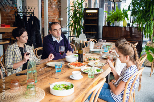 A young family with kids in a cafe, the parents are drinking wine. © Anna Kosolapova