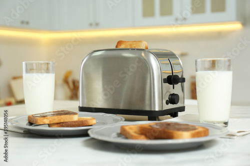 Modern toaster, bread slices with chocolate cream and glasses of milk on white marble table in kitchen
