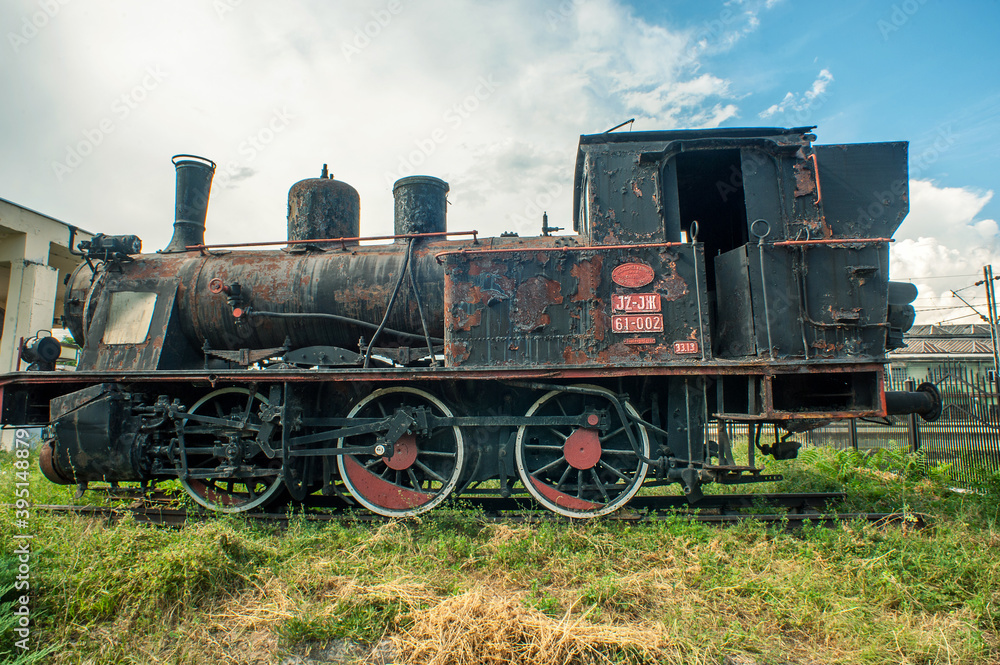 Naklejka premium An old rusty locomotive in front of the main train station of the city.