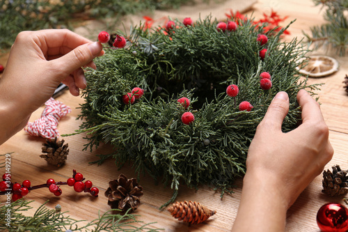 Florist making beautiful Christmas wreath with berries at wooden table, closeup
