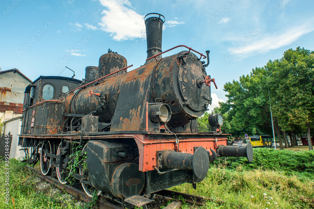 Naklejka premium An old rusty locomotive in front of the main train station of the city