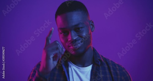 Handsome african american guy pointing at his head, gesturing think yourself, studio shot in neon lights, close up