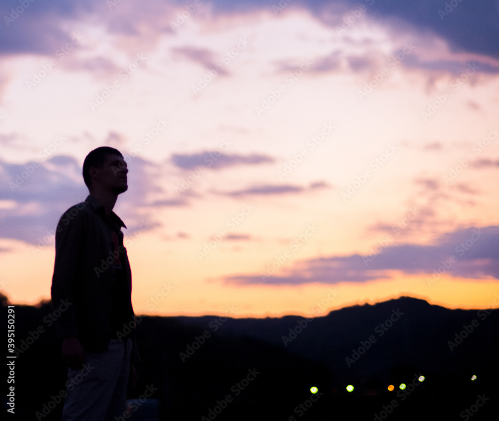 Man silhouette in front of a beautiful purple cloudy sky and orange sun rays 