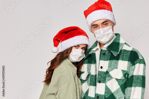 Man and woman in medical masks Christmas hats hugs cropped studio view