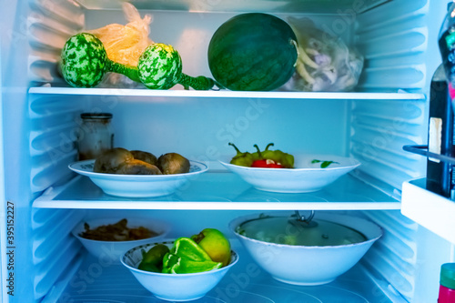 Shelves of an open frige refrigerator with different food, cooked food in pot and plastic container. photo