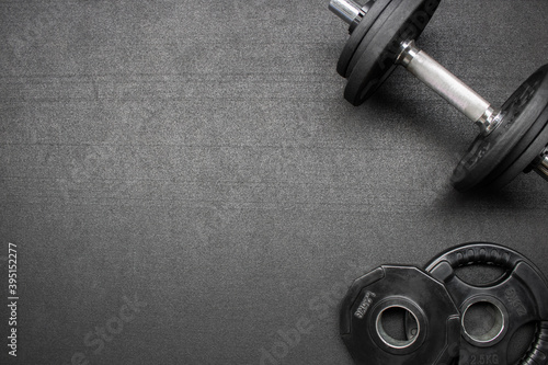 Barbell and dumbbells on the floor at the gym. Top down view flat lay with bodybuilding equipment on a black background and empty space for text. Fitness, weight training or healthy lifestyle concept