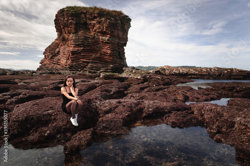 Girl posing with a n elegant black dress at a rocky cove of the basque coast. 