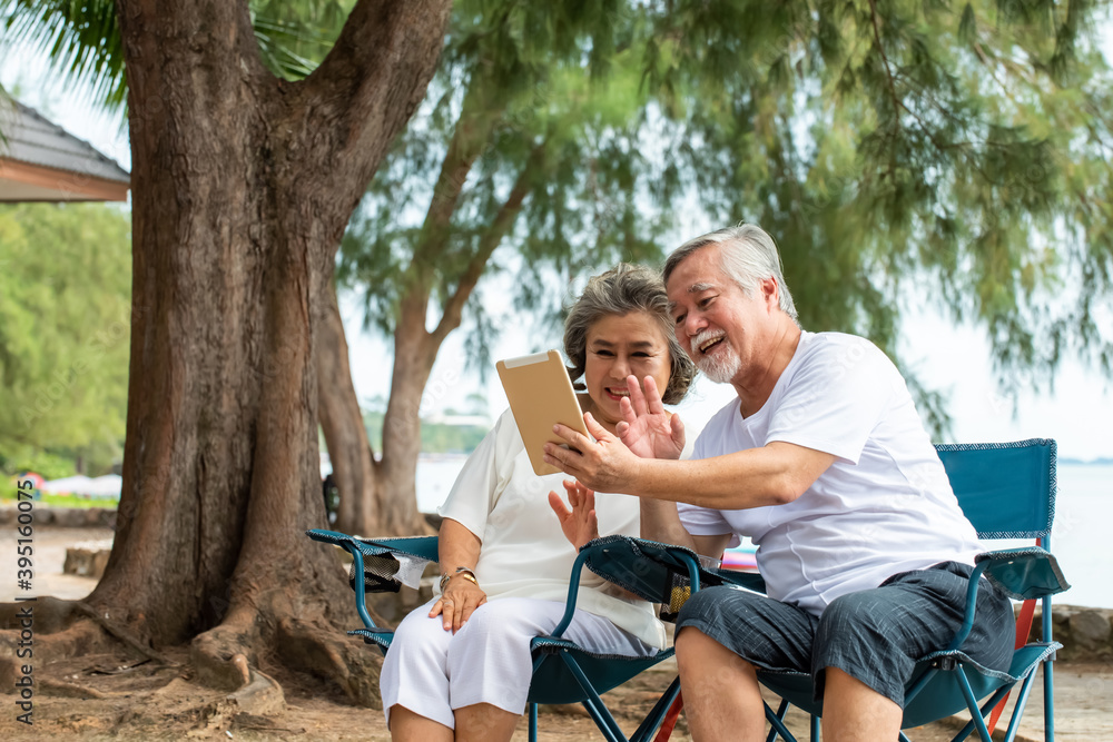 Happy family Asian senior couple using tablet computer with internet video call with their family or friend on the beach in summer day. Healthy retired man and woman enjoy with summer holiday vacation Happy family Asian senior couple using tablet computer with internet video call with their family or friend on the beach in summer day. Healthy retired man and woman enjoy with summer holiday vacation