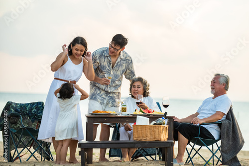 Group of Happy multi generation Asian family enjoy dinner party together on the beach at sunset. Parents with senior grandparents and cute child girl relax and having fun on summer holiday vacation © CandyRetriever 