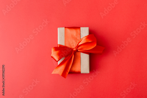 Present box with red bow on red background. Flat lay, top view.