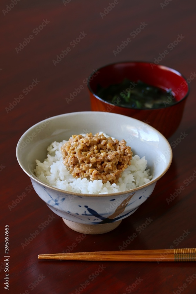 A close up shot of some finely chopped fermented soybeans on freshly cooked white rice in a ceramic rice bowl.