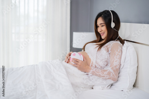 pregnant woman listening to fetal heart sound through headphones on bed © geargodz