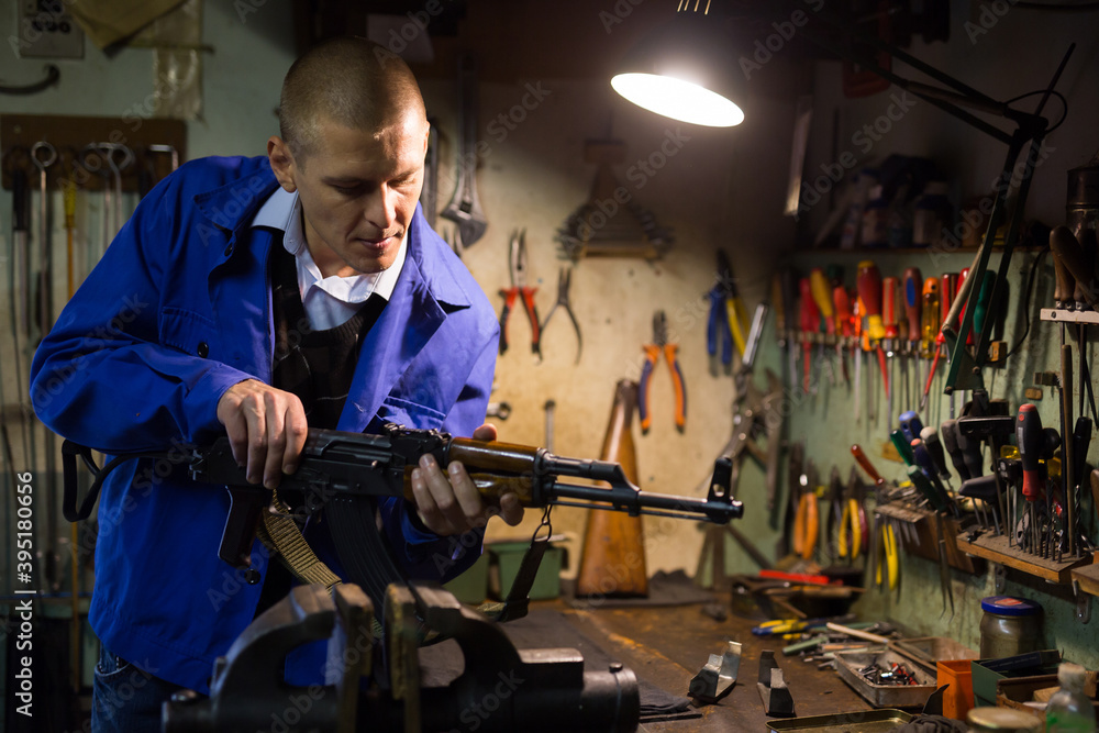 Qualified gunsmith performing maintenance of Kalashnikov assault rifle in weapons workshop.