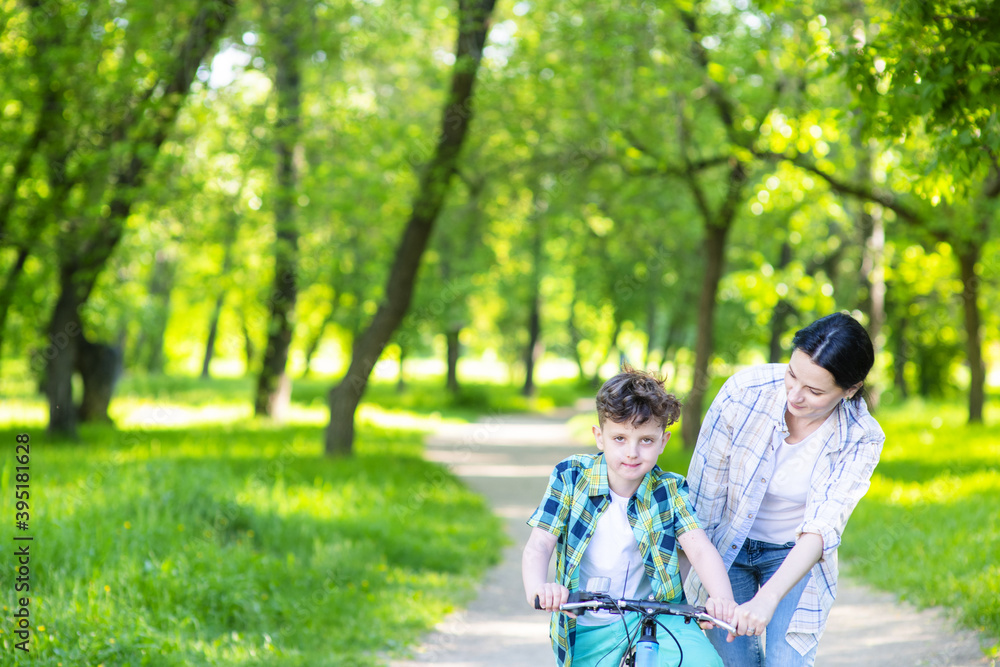 Mom helping her son learn to ride a bike in a summer park. Mom helping her son learn to ride a bike in a summer park.
