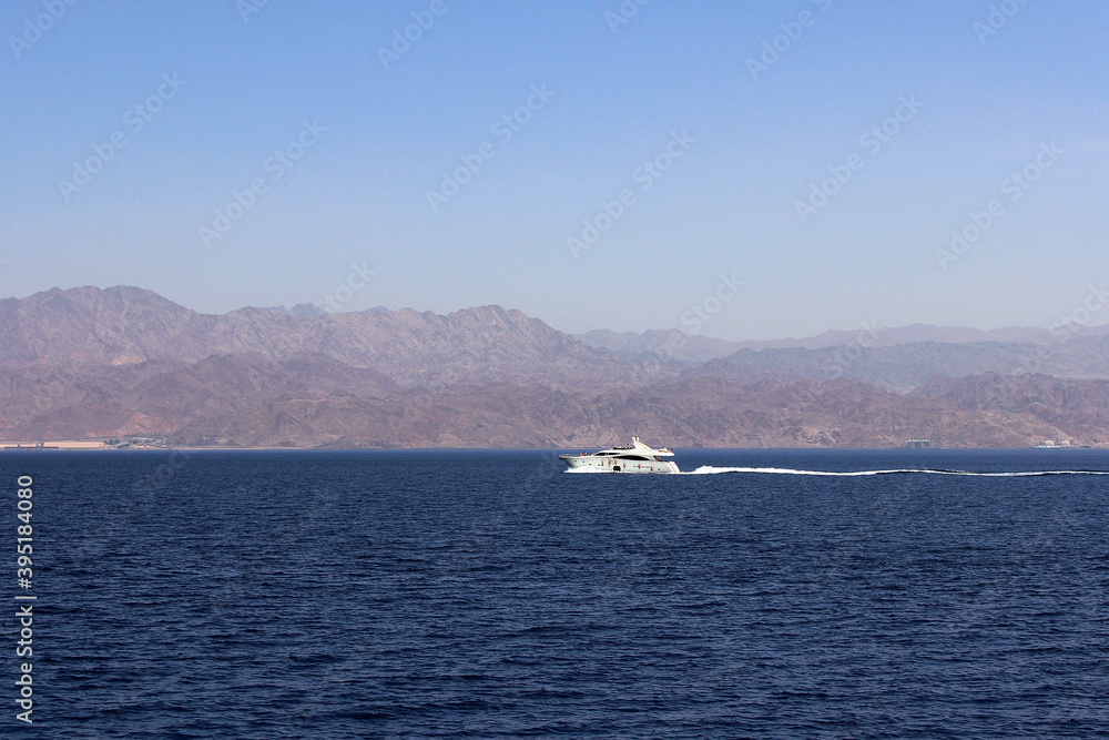 White boat in the red sea in Eilat against the background of the pink mountains of Jordan. Azure-blue sea with pink mountains on a Sunny afternoon in Eilat. Israel.
