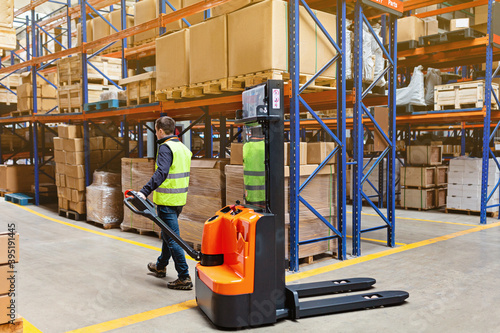 Storehouse employee in uniform working on forklift in modern automatic warehouse. Boxes are on the shelves of the warehouse. Warehousing, machinery concept. Logistics in stock. photo