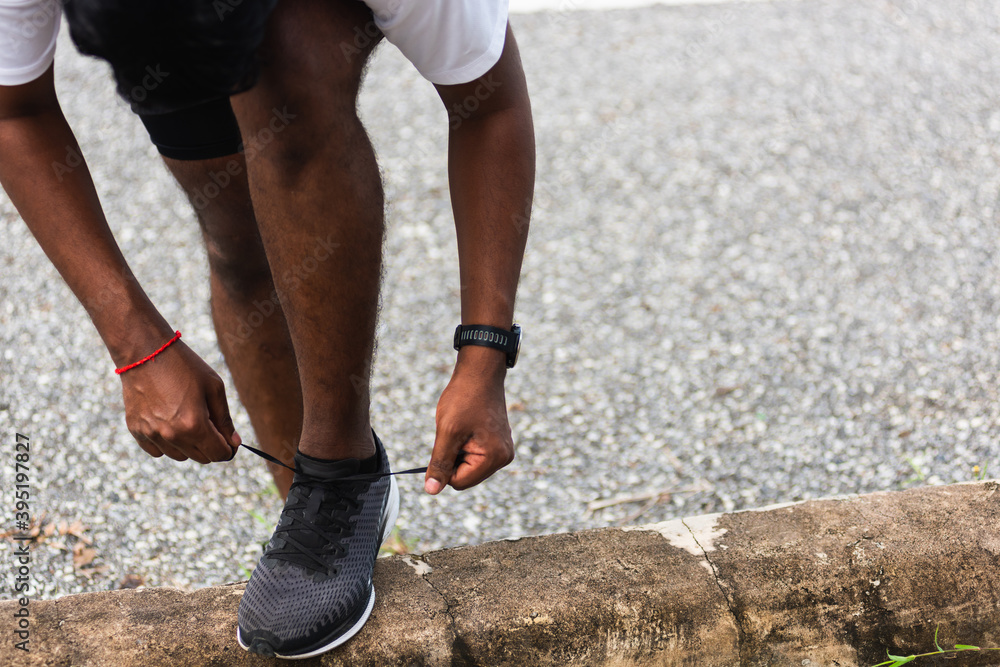 Close up Asian sport runner black man wear watch stand step on the footpath trying shoelace running shoes getting ready for jogging and run outdoor street health park, healthy exercise workout concept Close up Asian sport runner black man wear watch stand step on the footpath trying shoelace running shoes getting ready for jogging and run outdoor street health park, healthy exercise workout concept