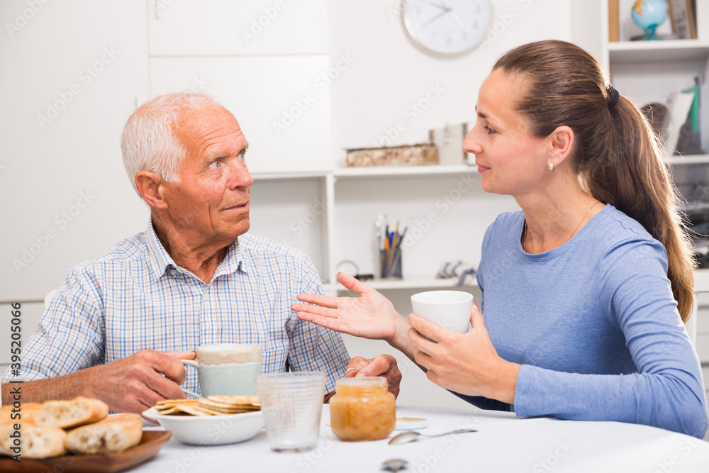 Elderly father and adult daughter talk and drink tea in the kitchen