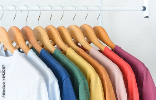 close up collection of colorful t-shirts hanging on wooden clothes hanger in closet or clothing rack over white background, copy space